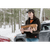 A young woman carrying firewood in the winter with a car in the background. She is wearing the Stormy Kromer Lighthouse Jacket in evergreen plaid.