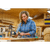 Lady with long curly hair wearing a blue and pink plaid Weekender flannel button up shirt in a woodshop.