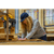 Lady with long curly hair wearing a blue cap and gray Base Camp Pullover fleece working in a woodshop