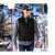 Man wearing a cap and wool vest over light gray shirt walking in town.