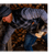 Man picking up logs wearing a vest, mitten, and warm hat.