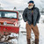 Man standing next to a red truck with a plow in the wintertime wearing a Wool Overshirt and a wool cap