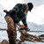 Man using a chainsaw outside in the winter cutting logs in a Frontier Shirt Jack and Original Cap