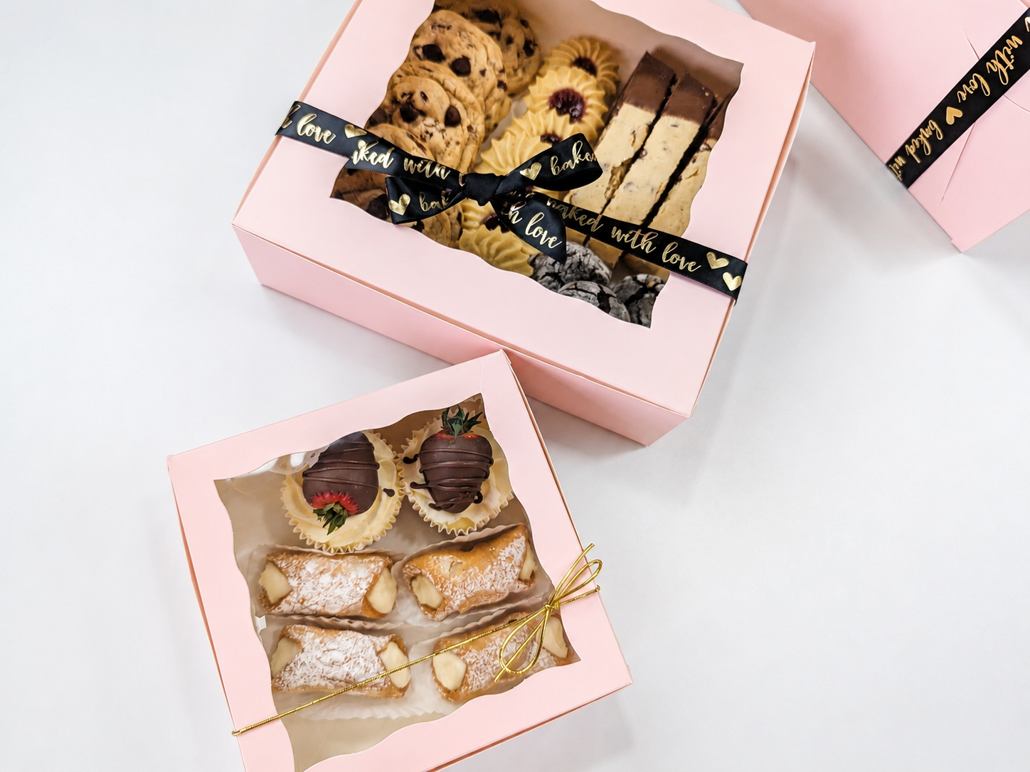 Two soft pink bakery boxes filled with decorated cookies and pastries, showing gift-ready presentation.
