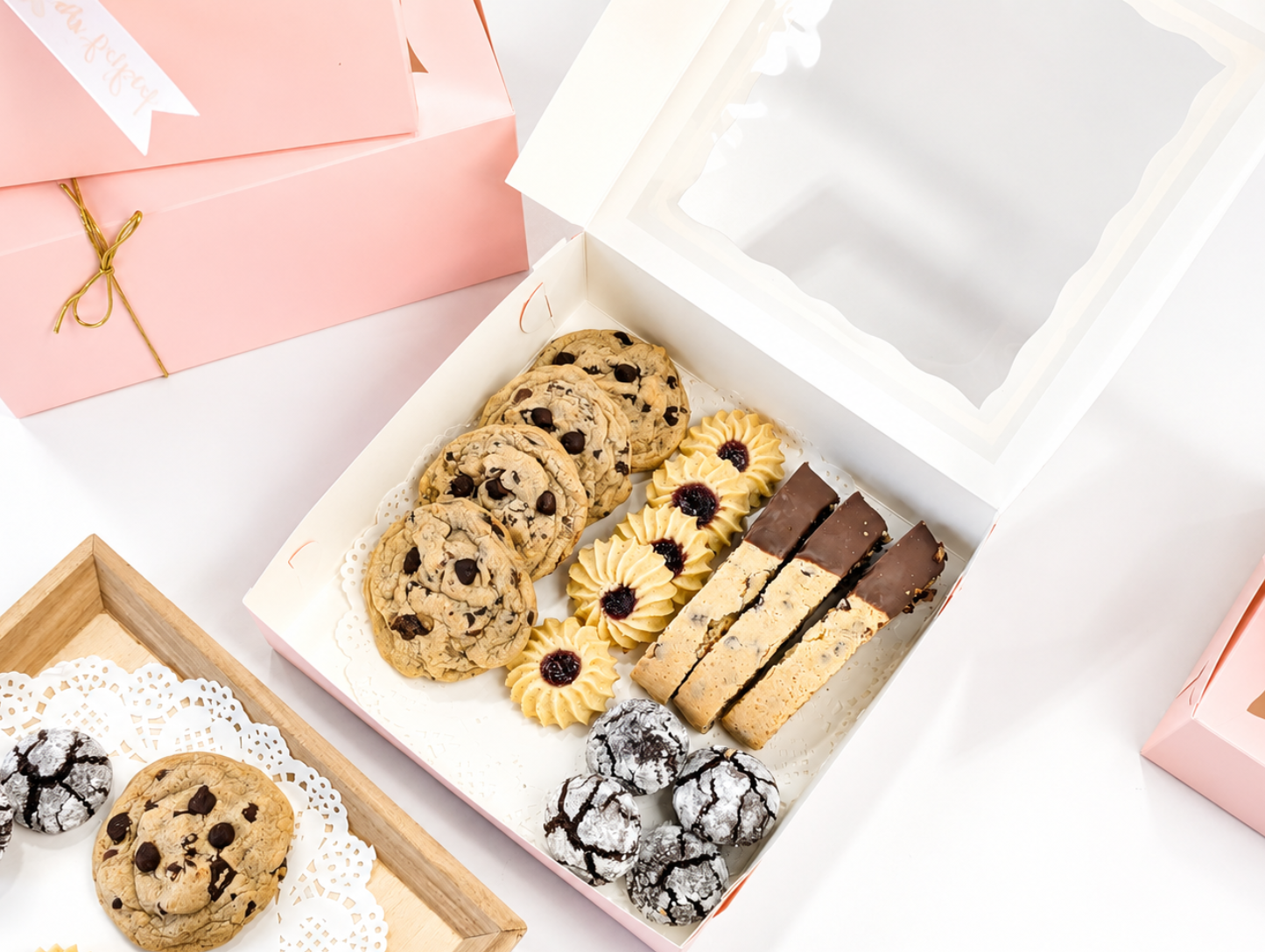 An open pink bakery box filled with cookies and dessert bars, showing the roomy interior and clear presentation of the treats.