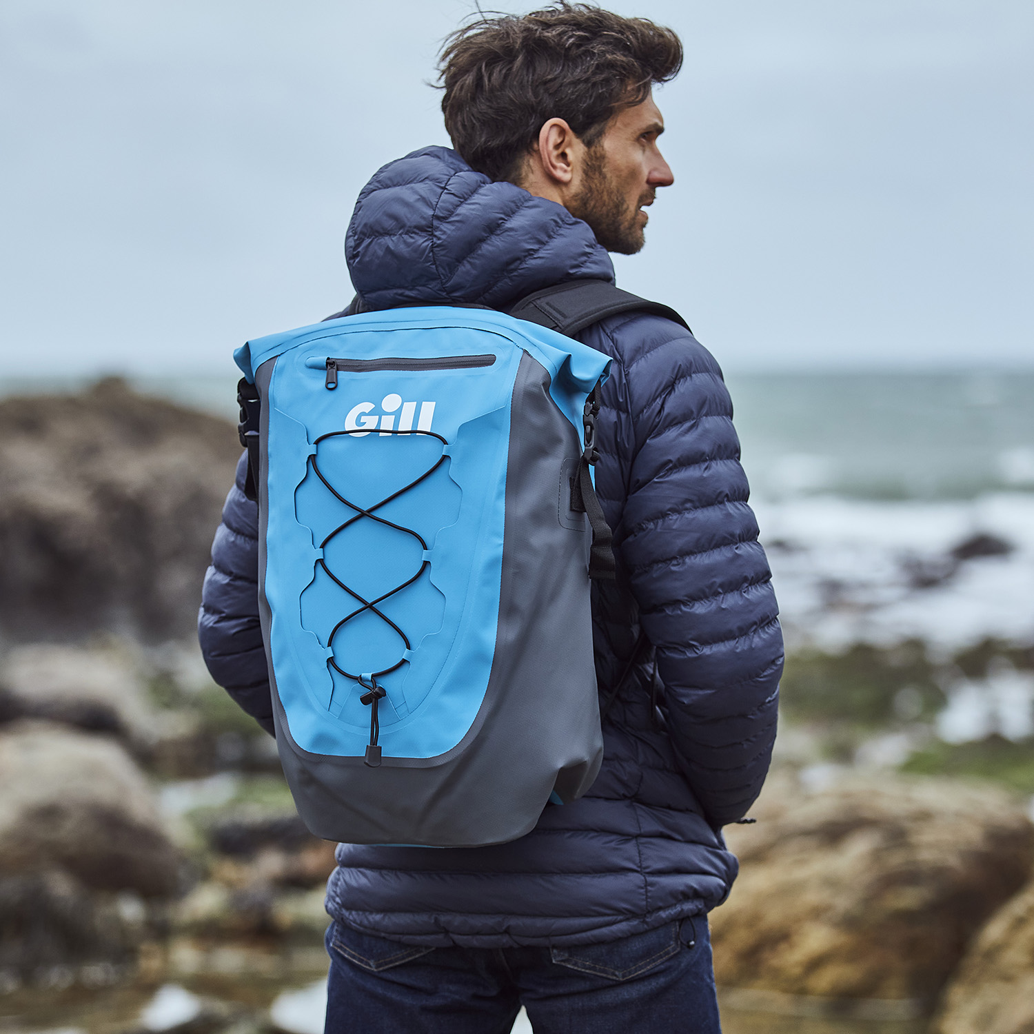 Man standing looking towards the sea wearing a Gill Voyager Kit Pack in Blue Jay 