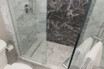 Curbless tile shower with marble-look walls, glass enclosure and linear drain
