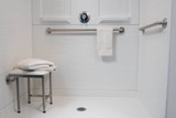 ADA compliant folding shower seat with legs, placed in a white tiled shower, accompanied by towels and grab bars
