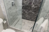Curbless tile shower with marble-look walls, glass enclosure and linear drain