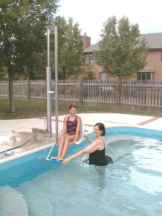 Aquatic Access IGAT-180 pool lift in use, assisting a woman into the pool while another person supports her