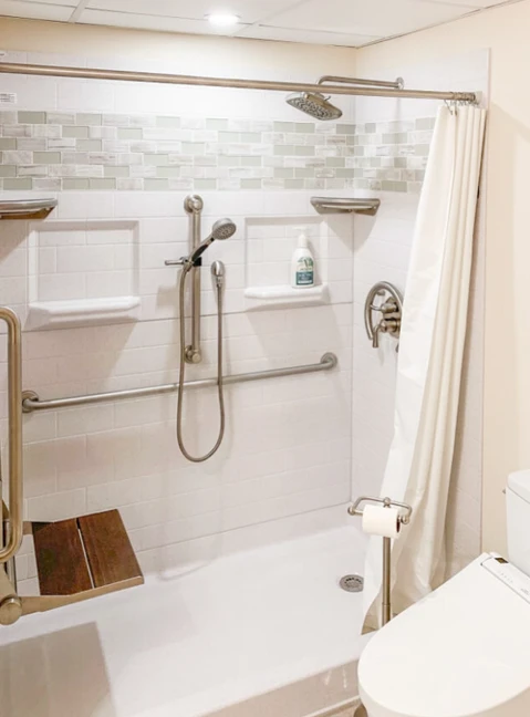 Curved shower curtain rod installed in accessible bathroom with safety grab bars, handheld shower