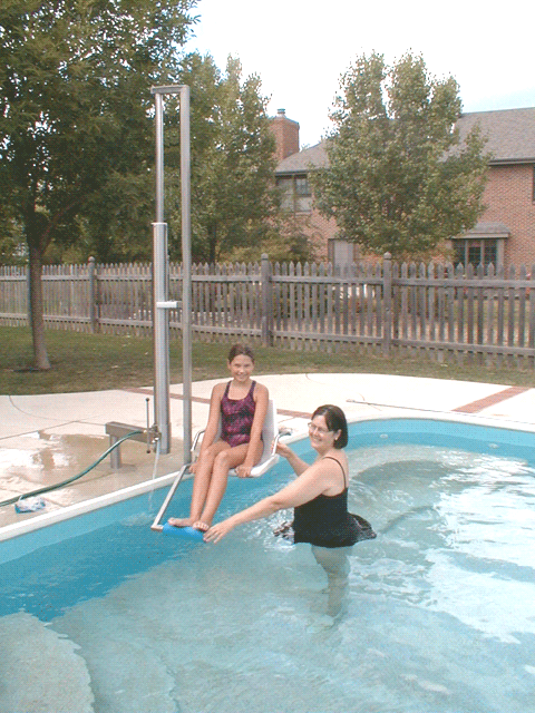 Aquatic Access IGAT-180 pool lift in use, assisting a woman into the pool while another person supports her