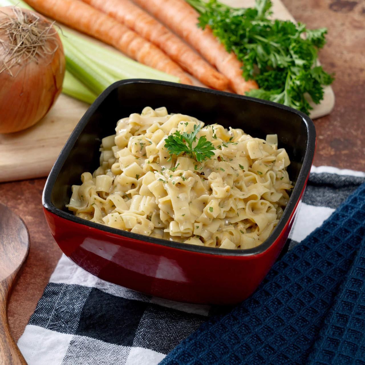 ReadyWise 52 Serving Emergency Food - Prepper Pack Bucket, prepared macaroni and cheese dish garnished with parsley in a red bowl placed on a black and white cloth with fresh vegetables in the background.