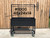Heavy-duty black metal charcoal grill with a large firebox and four rolling casters.