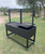 Black Santa Maria grill on wheeled cart outdoors; dual adjustable grates and rugged design.