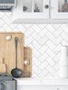 Kitchen backsplash featuring Carrara White Herringbone composite tiles behind a countertop with wooden cutting boards.