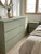 A sunlit, cozy bedroom featuring a large six-drawer dresser and a matching nightstand, both beautifully finished in Smokey Sage Green Fabric Vinyl Wrap SSGF988.
