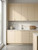 A sunlit, modern kitchen featuring sleek, handle-less cabinets elegantly wrapped in Matte Textured Creamy Magnolia Vinyl Wrap MTCM72, complemented by a light marble backsplash and countertop.