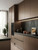 A modern kitchen design showcasing tall pantry cupboards and base units wrapped in Satin Textured Copper Brown Vinyl Wrap STCB33, beautifully contrasted against a moody black concrete backsplash, built-in black ovens, and copper cookware.