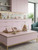 A stylish, modern kitchen or cafe interior featuring wall cabinets and a central display table elegantly finished in Matte Textured Pale Pink Vinyl Wrap MTPP61, perfectly accented with brass trim, marble surfaces, and pastel macarons.