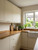 A bright, welcoming kitchen featuring flat-panel upper and lower cabinets seamlessly wrapped in Ivory Stucco Plaster Vinyl Wrap ISP14. The soft, textured ivory cabinets are beautifully complemented by natural wood countertops, a classic white farmhouse sink, and elegant brass handles.