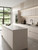 A bright, modern kitchen featuring sleek, flat-panel handleless cabinets and a large central island, all flawlessly wrapped in Matte Textured Eggshell Cream Vinyl Wrap MTEC49. The soft, warm cream finish is elegantly paired with a light grey stone countertop, a matte black faucet, and warm under-cabinet LED lighting.