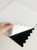 Hand peeling the white protective backing off a copper mosaic peel and stick composite wall tile to reveal the adhesive.