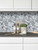 Modern kitchen counter featuring white cabinets, dark countertop, salt and pepper shakers, and a brushed aluminium herringbone tile backsplash.