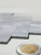 Macro detail showing the brushed metallic texture and rigid edge of the aluminium herringbone composite wall tile next to a coin.