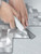 Person scoring and cutting an aluminium metal herringbone peel and stick composite wall tile using a metal ruler and utility knife.