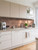 Modern kitchen featuring crisp white cabinets, light countertops, and a striking 3D copper geometric peel and stick tile backsplash.