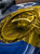 A detailed close-up of a professional auto-detailer in black gloves carefully applying a vibrant, glossy yellow tint film to the sophisticated multi-projector LED headlight of a deep blue Porsche 911 (992), using a gray squeegee tool to smooth the surface and eliminate air bubbles, creating a custom yellow-lens look.