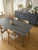 A bright, contemporary dining room featuring a sleek minimalist table flawlessly wrapped in Layed Grey Oak Wood Vinyl Wrap, paired with light wood chairs.