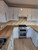 An impressive kitchen makeover 'after' shot, displaying clean white upper and lower cabinets with a continuous, water-resistant countertop upgraded using Layed White Oak Wood Vinyl Wrap.