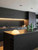 A sleek, moody modern kitchen featuring matte black cabinetry seamlessly contrasted with a stunning illuminated backsplash and a large center island wrapped in Layed Calatorao Black Marble Vinyl Wrap.
