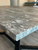 A macro close-up of a tabletop edge wrapped flawlessly in Layed Orobico Grey Marble Vinyl Wrap, showing a professional, seamless corner fold and realistic stone texture.