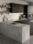 A sleek, moody modern kitchen showcasing matte black cabinetry perfectly contrasted by a large center island, countertops, and a backsplash wrapped in Layed Industrial Metallic Concrete Vinyl Wrap.