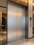A modern commercial lobby featuring elevator doors seamlessly upgraded with Layed Brushed Metal Silver Aluminium Vinyl Wrap, showcasing its realistic stainless steel finish and linear texture.