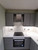 Kitchen area showing upper and lower cabinets wrapped in Matte Textured Rock Grey vinyl, paired with a black countertop and white tiled backsplash.