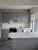 Upcycled kitchen displaying lower and upper cabinets resurfaced in rock grey matte vinyl wrap, contrasting with white marble countertops and backsplash.