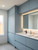 A contemporary bathroom featuring sleek, handleless vanity and storage cabinets beautifully transformed using Layed Matte Silk Duck Egg Vinyl Wrap, illuminated by a modern backlit mirror.