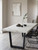 A modern dining room featuring a table beautifully transformed with Layed Calacatta White Marble Vinyl Wrap, showcasing bold grey veining.