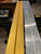 A side-by-side comparison showing a raw silver aluminum extrusion next to a trim piece seamlessly wrapped in Satin Textured Gold vinyl film.
