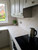 Close-up of a bright kitchen countertop and protective backsplash seamlessly covered in Layed Crema Marble Vinyl Wrap, showing a professional finish next to a black glass stovetop.