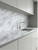 A sleek, modern kitchen with minimalist grey cabinets, perfectly contrasted by a continuous countertop and protective backsplash covered in Layed Volakas White Marble Vinyl Wrap.