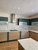 A bright, contemporary kitchen featuring a two-tone design of dark green and warm wood cabinets, unified by continuous countertops and a backsplash flawlessly upgraded with Layed White Terrazzo Vinyl Wrap.