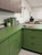 A corner classroom desk and built-in storage cabinets smoothly resurfaced with Layed Matte Textured Forest Green Vinyl Wrap MTFG66, topped with books and a potted plant.