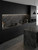 A sleek, modern kitchen featuring matte black cabinetry seamlessly contrasted with a stunning illuminated backsplash and island wrapped in Layed Lombarda Grey Marble Vinyl Wrap.