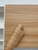Layed Natural Pine Wood Vinyl Wrap partially unrolled against a white shelving unit, highlighting the authentic tactile wood grain pattern.