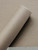 A close-up view of Layed Caramel Fabric Vinyl Wrap partially unrolled, highlighting the intricate, warm brown woven textile pattern and premium matte finish.
